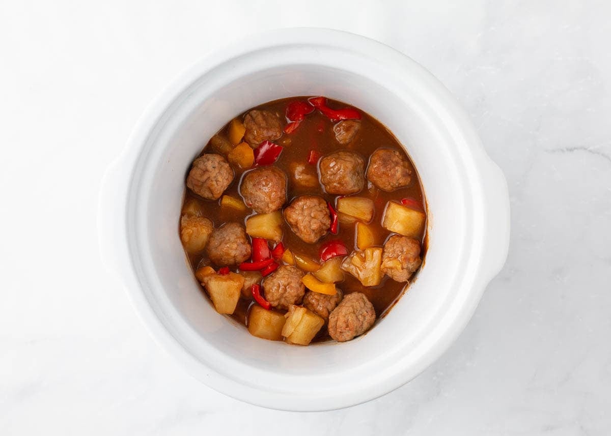 Hawaiian meatballs with pineapple and bell peppers cooking in BBQ sauce in a crockpot.