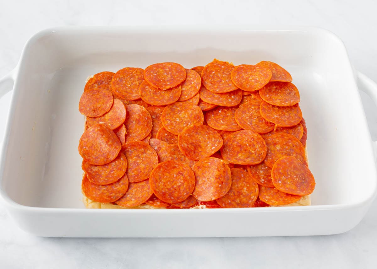 Image 2 (pepperoni layer):
Pepperoni slices layered over pizza sauce on Hawaiian rolls in a baking dish.