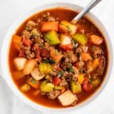 Vegetable beef soup in a white bowl with a spoon.