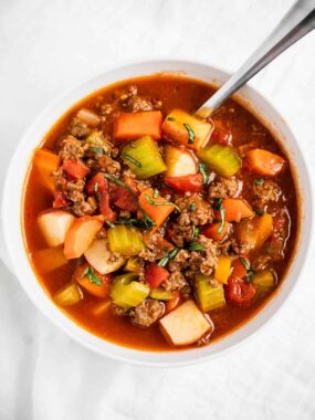 Vegetable beef soup in a white bowl with a spoon.