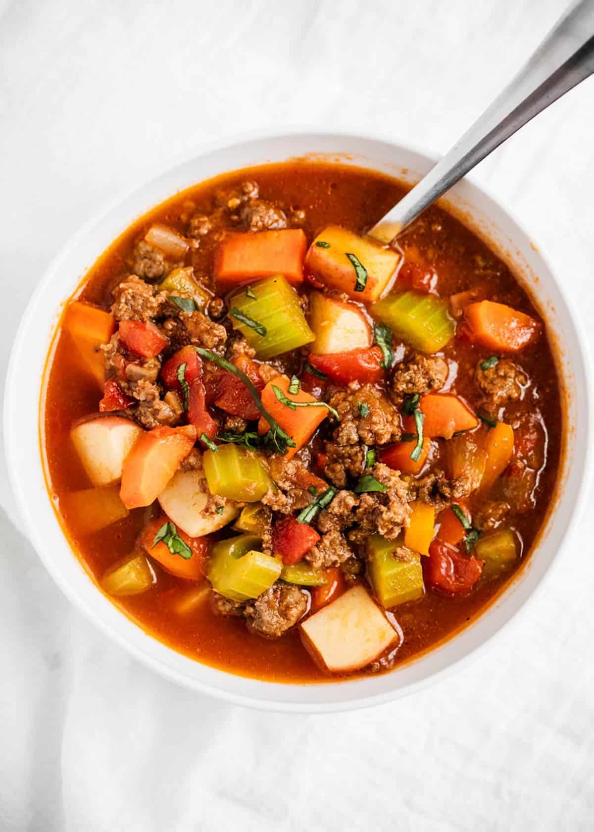 Vegetable beef soup in a white bowl with a spoon.