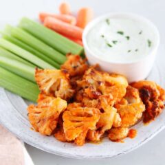 Roasted buffalo cauliflower wings on a plate with celery and ranch dressing.