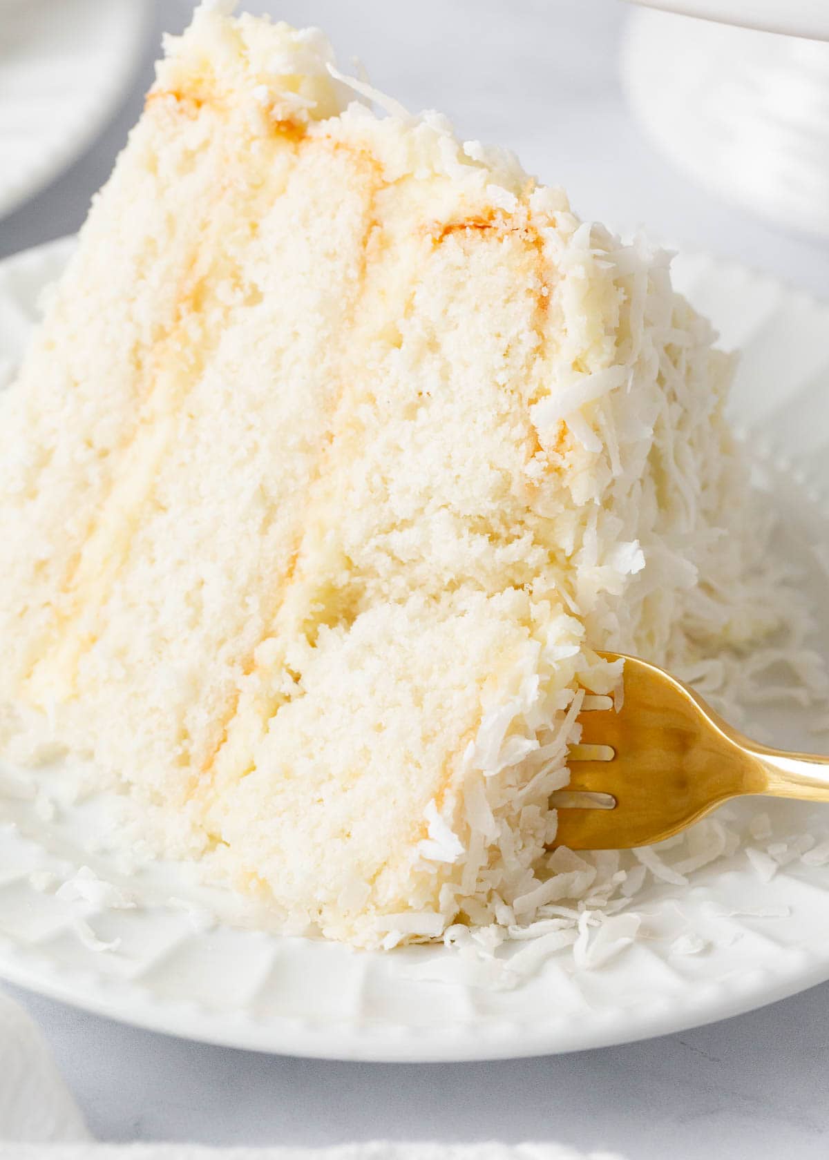 Taking a bite of coconut cake on a white plate.