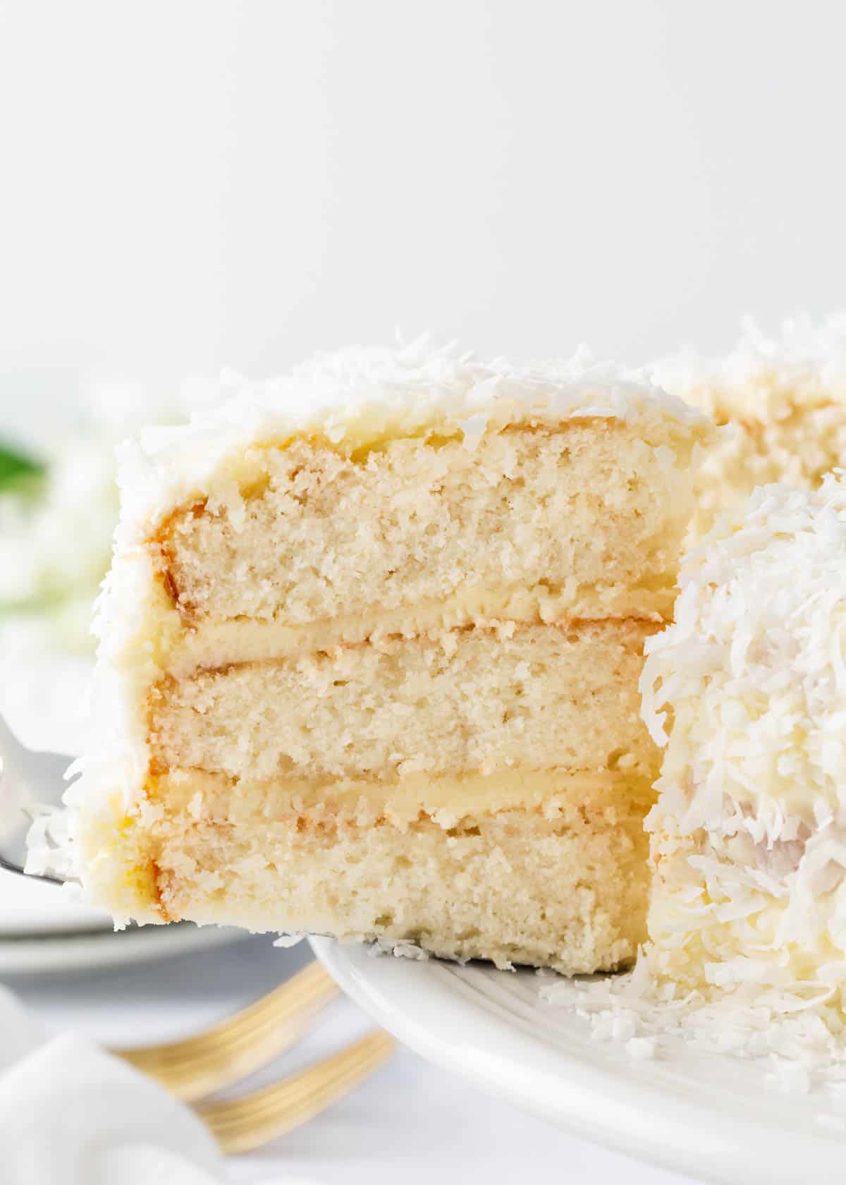 This simple and moist coconut cake is triple layered with a luscious coconut cream cheese frosting and garnished with sweet coconut flakes. It's elegant, easy and perfectly suited for any occasion! Slice of coconut cake.