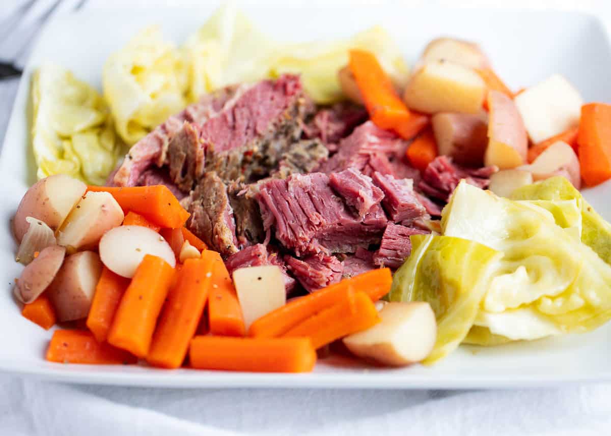 Slow cooked tender corned beef and cabbage on plate with carrots and potatoes.