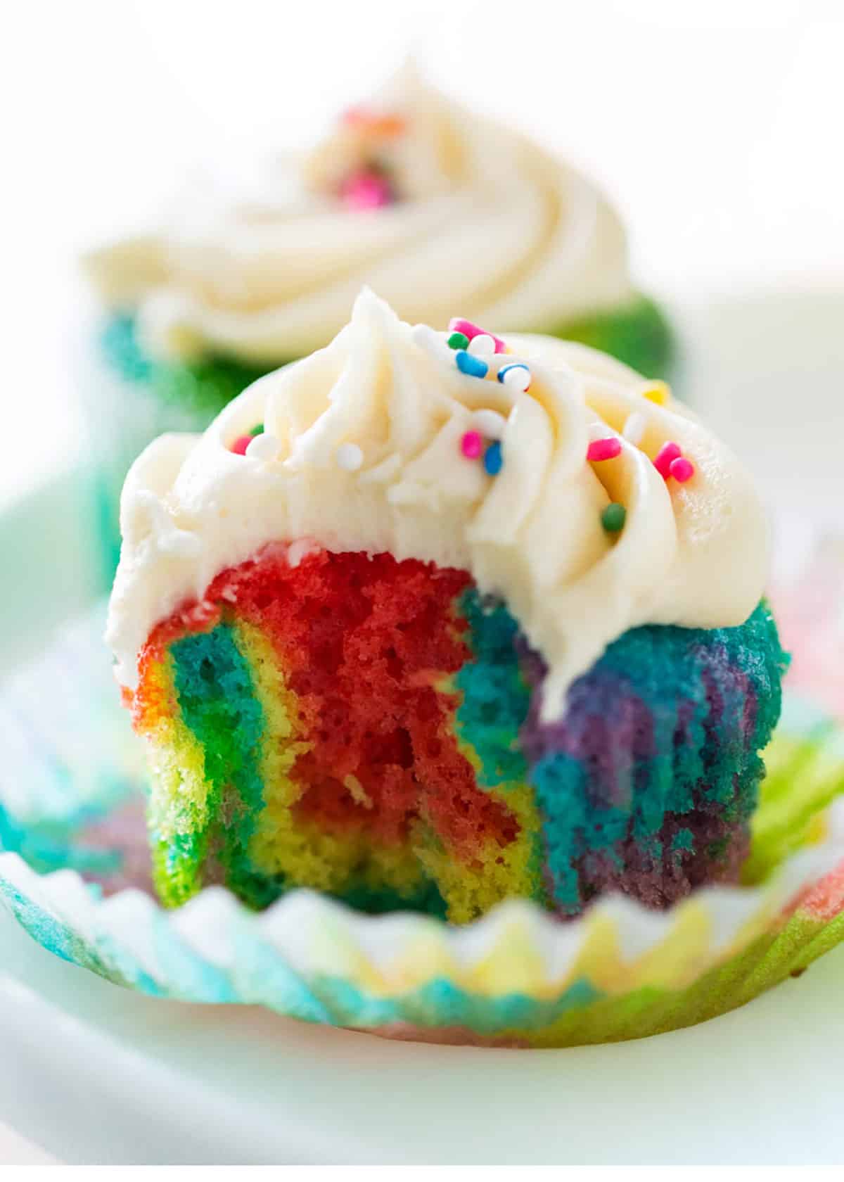 These rainbow cupcakes have layers of vibrant rainbow colors and are topped with buttercream frosting. Easy to make with doctored cake mix, they are festive for St. Patrick's Day or any party! Rainbow cupcake biten into.