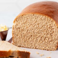 A sliced homemade whole wheat bread loaf with a soft fluffy crumb, served with butter.