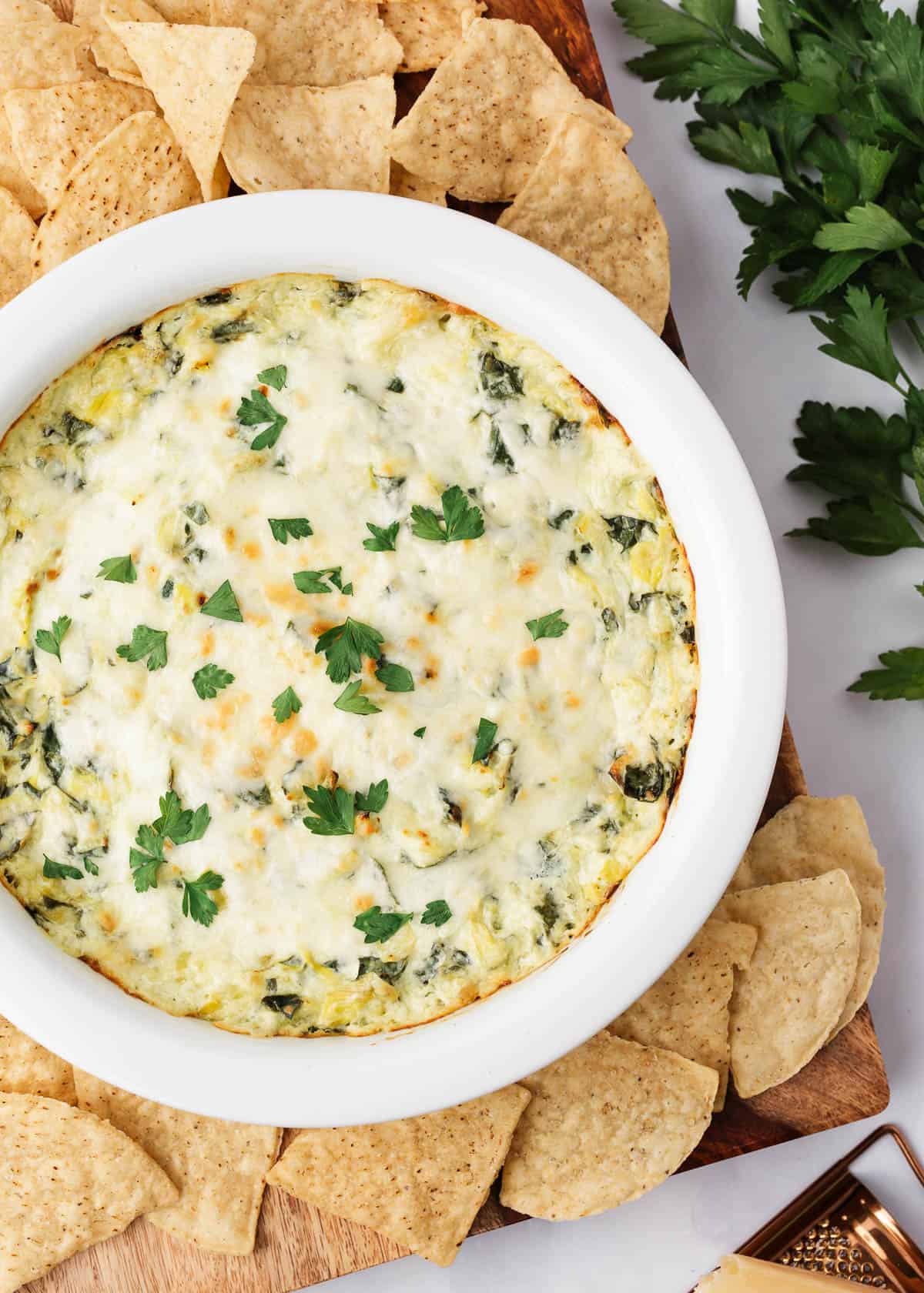 Spinach artichoke dip in a white pie dish with chips.
