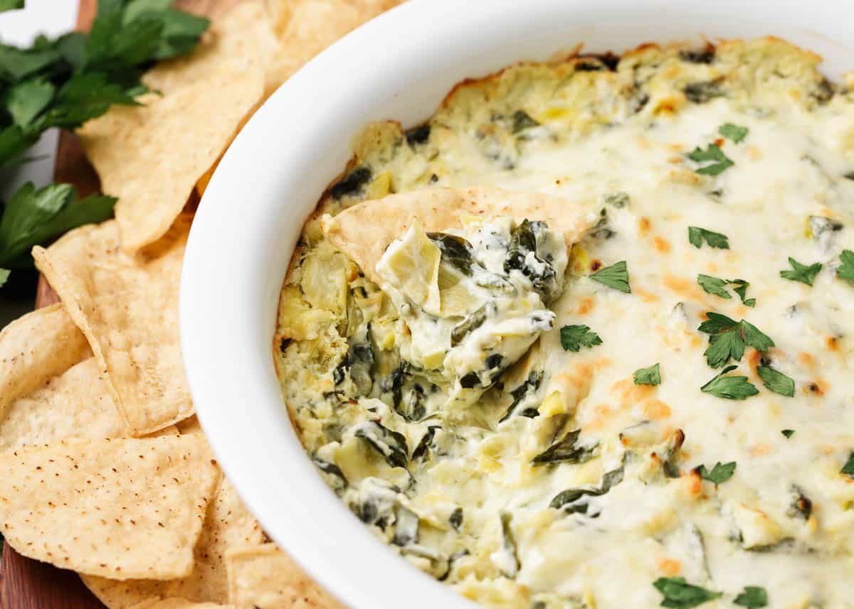 Spinach artichoke dip baked in a white baking dish.