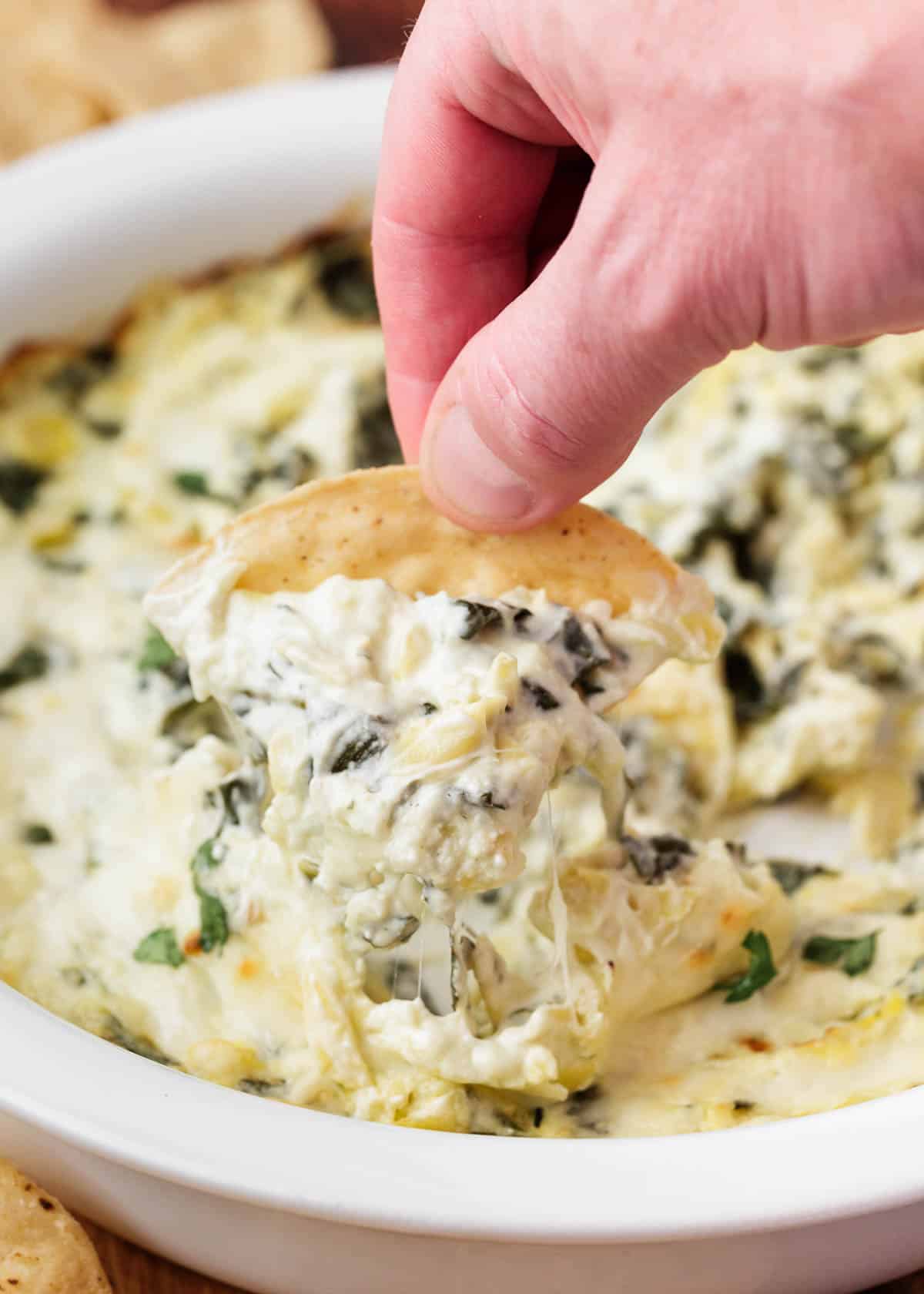 This baked spinach artichoke dip is a rich and creamy savory appetizer loaded with spinach, artichokes and cheeses then baked until golden and bubbly. It's an irresistible crowd-pleasing dip perfect for any party! Spinach artichoke dip on a tortilla chip.