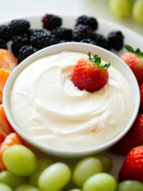 Marshmallow cream cheese fruit dip in a bowl with fresh fruit for dipping.