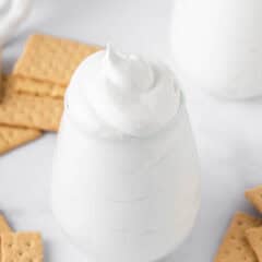Homemade marshmallow fluff piled high in a glass jar surrounded by graham crackers.