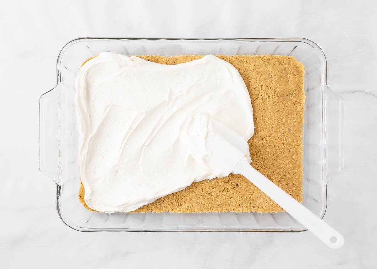 Cheesecake layer being smoothed over shortbread crust.