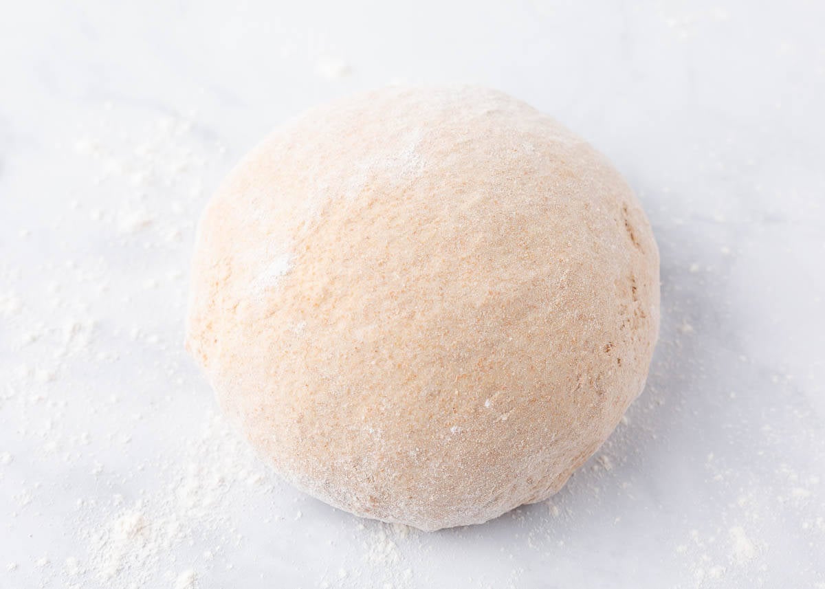 Wheat bread dough being kneaded and shaped into a ball.