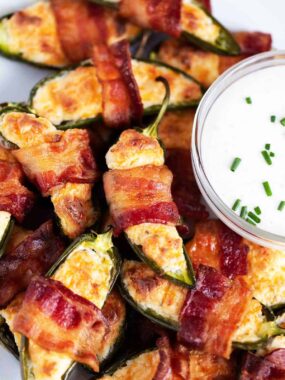Bacon-wrapped jalapeño poppers arranged on a white tray with ranch dipping sauce in the center.