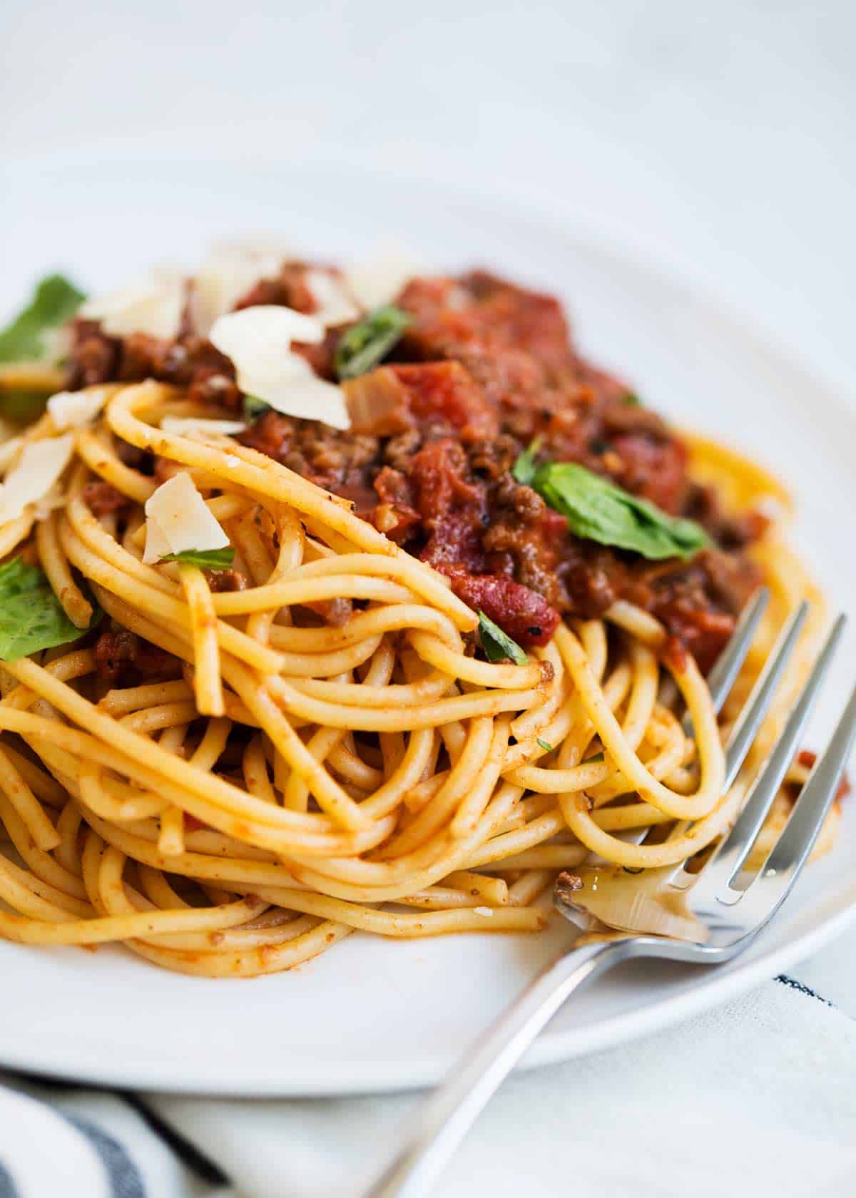 This spaghetti bolognese is an easier version of the classic Italian pasta dish! A thick homemade meat sauce is simmered with tomatoes, onion and savory herbs then served over spaghetti for a hearty meal! Spaghetti bolognese sauce with pasta on a white plate.