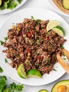 Barbacoa beef shredded on a plate with lime wedges.