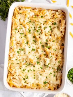 Whole chicken alfredo bake casserole in a baking dish with penne pasta, creamy sauce, melted cheese, and parsley.