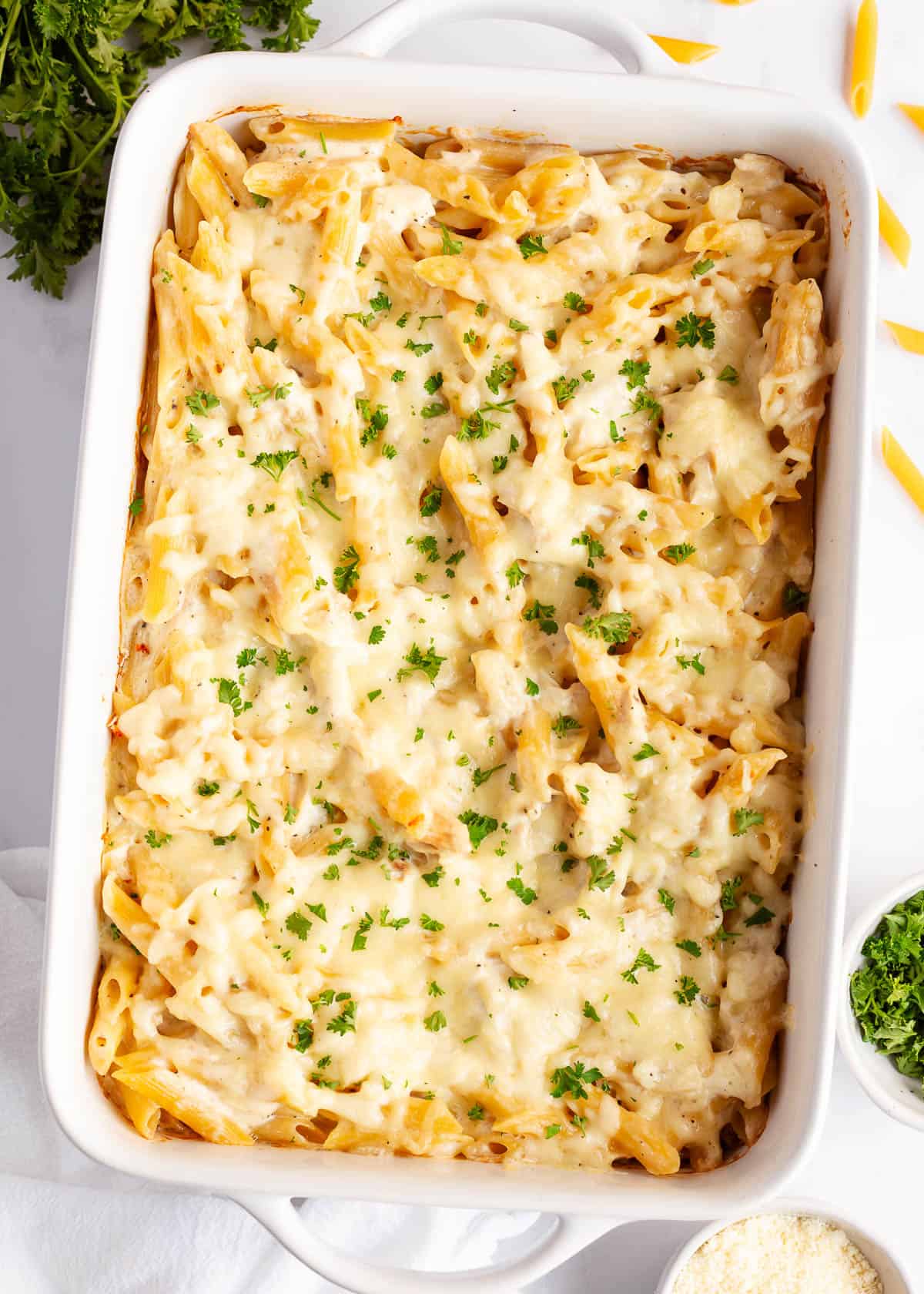 Chicken Alfredo bake is the perfect addition to your weeknight dinner rotation. With cooked chicken, Alfredo sauce and penne pasta, it's creamy, cheesy and comforting! Chicken alfredo bake in a white baking dish.