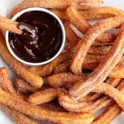 Churros on a plate being dipped in chocolate.