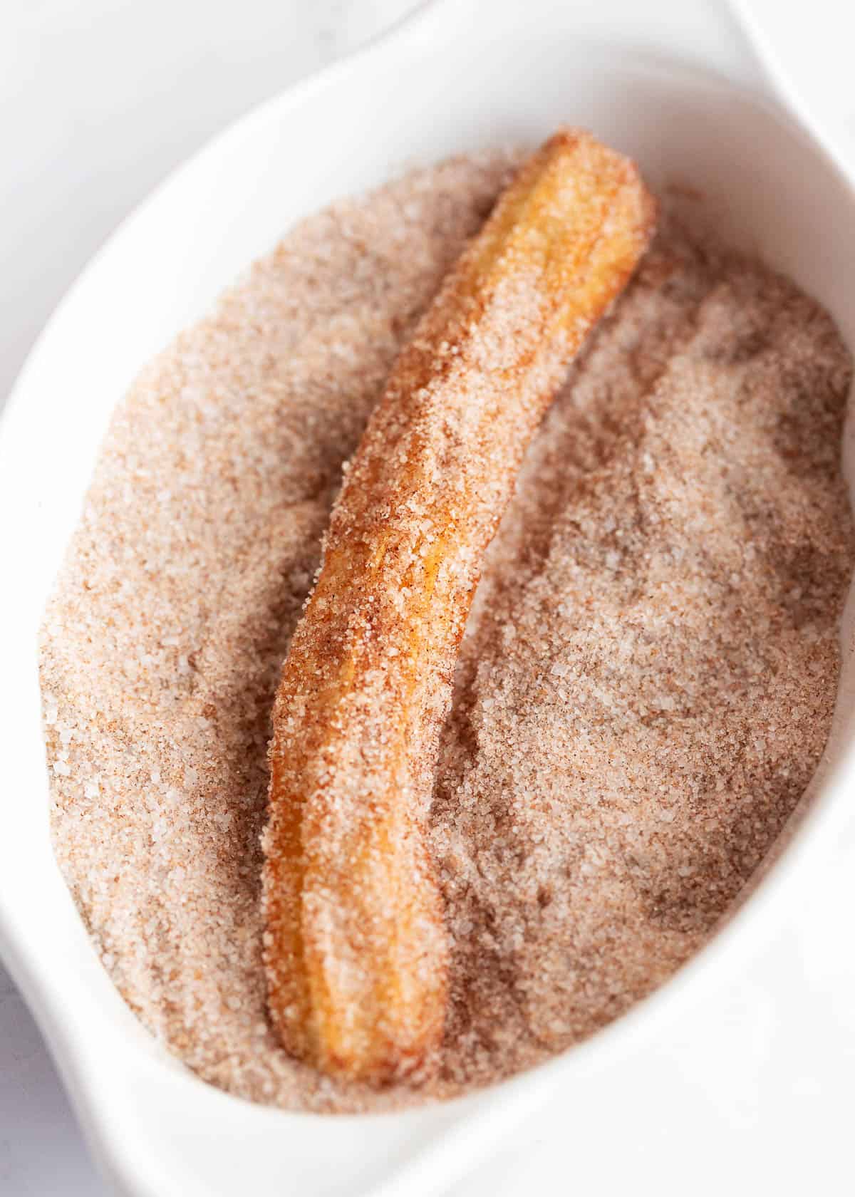 Churro being dipped in cinnamon.