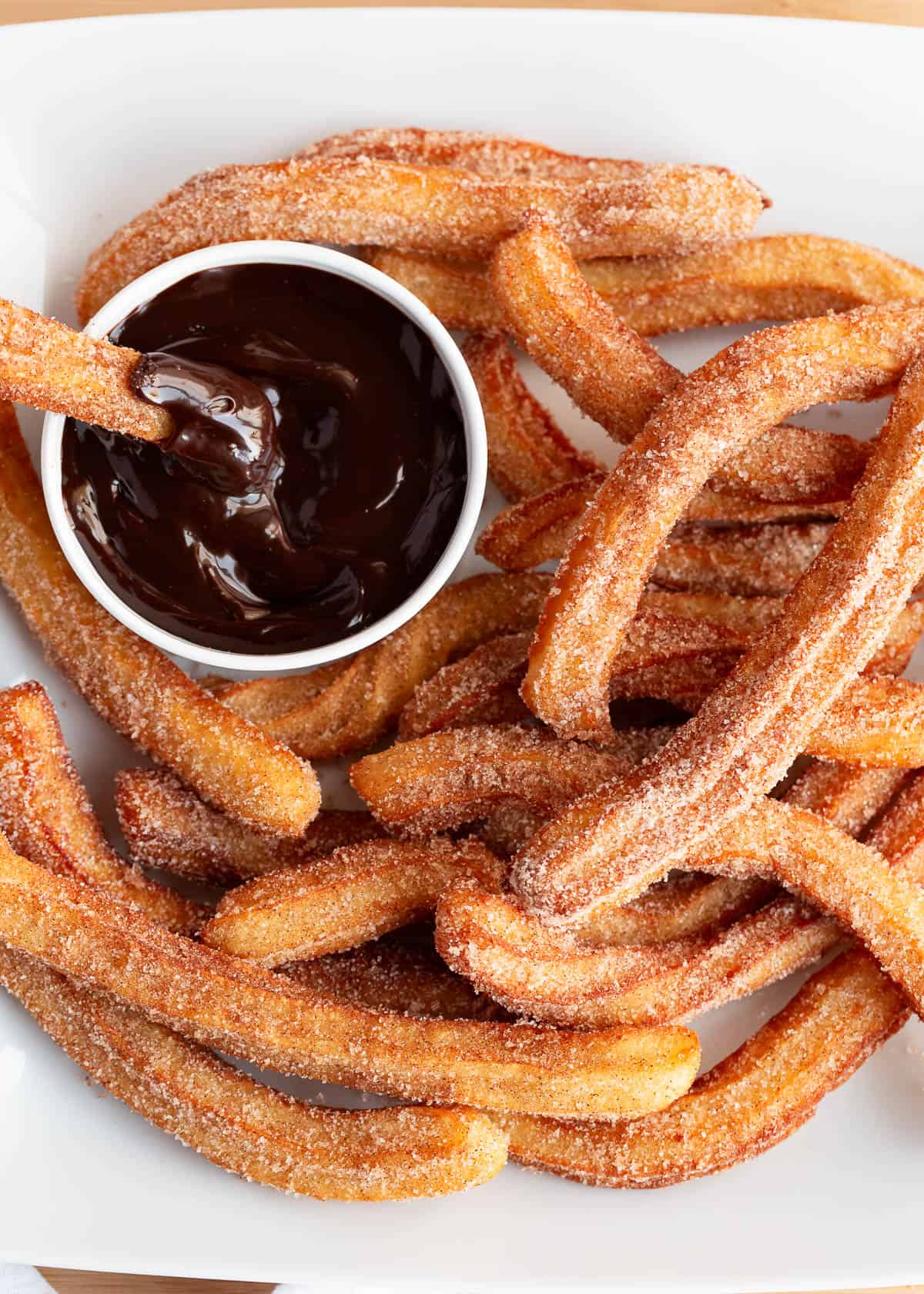 These easy homemade churros are to die for and are the perfect dessert! They are soft and tender on the inside and crispy on the outside. Churros on a plate being dipped in chocolate.