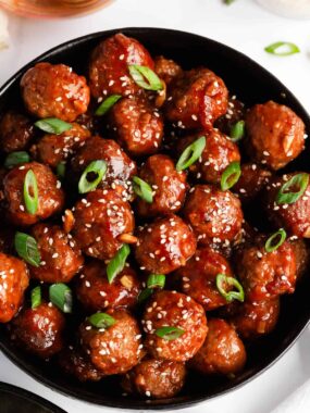 Honey garlic meatballs in a black bowl garnished with sesame seeds and green onions.