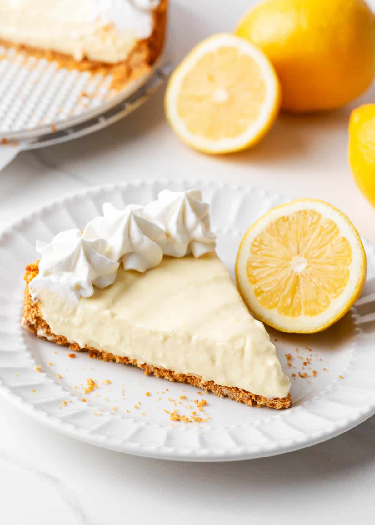 This lemon icebox pie is an old-fashioned, no-bake dessert made with a classic graham cracker crust and cream cheese, sweetened condensed milk and fresh lemon filling. Slice of lemon icebox pie on a white plate.