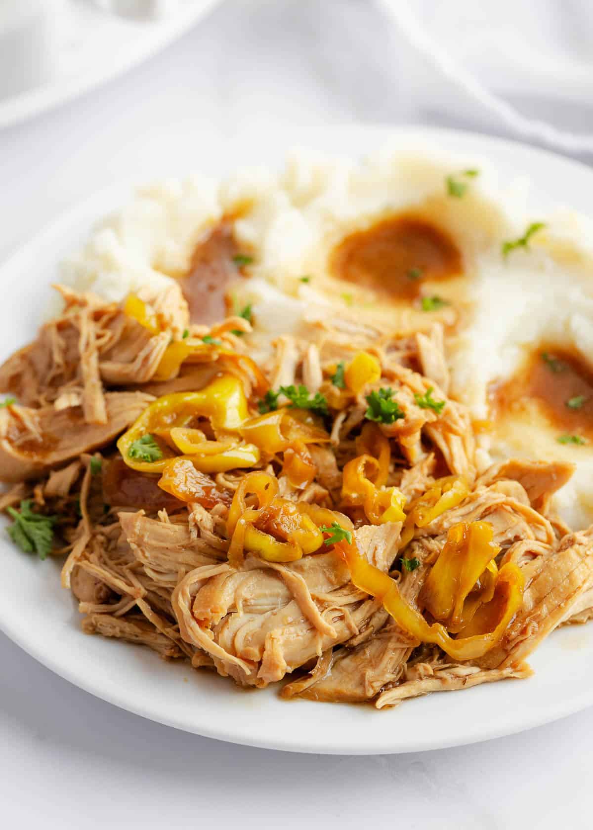 There's nothing quite like the savory flavors of this Mississippi chicken! It's easy to make with chicken, zesty pepperoncini, ranch and Au Jus gravy slow cooked in the crockpot until tender. Mississippi chicken and mashed potatoes on a plate.