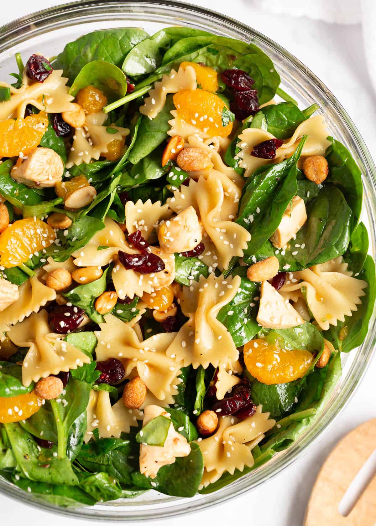 Flavorful spinach pasta salad with fresh spinach, crunchy nuts, shredded chicken, bowtie pasta, dried cranberries and juicy mandarin oranges tossed in a teriyaki dressing! Spinach pasta salad in a bowl.