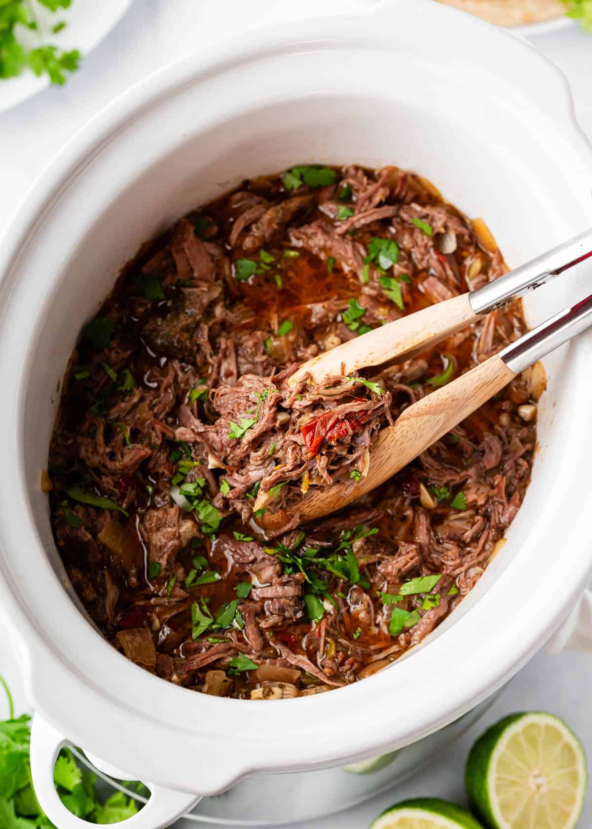 Beef barbacoa shredded in a crockpot with tongs.
