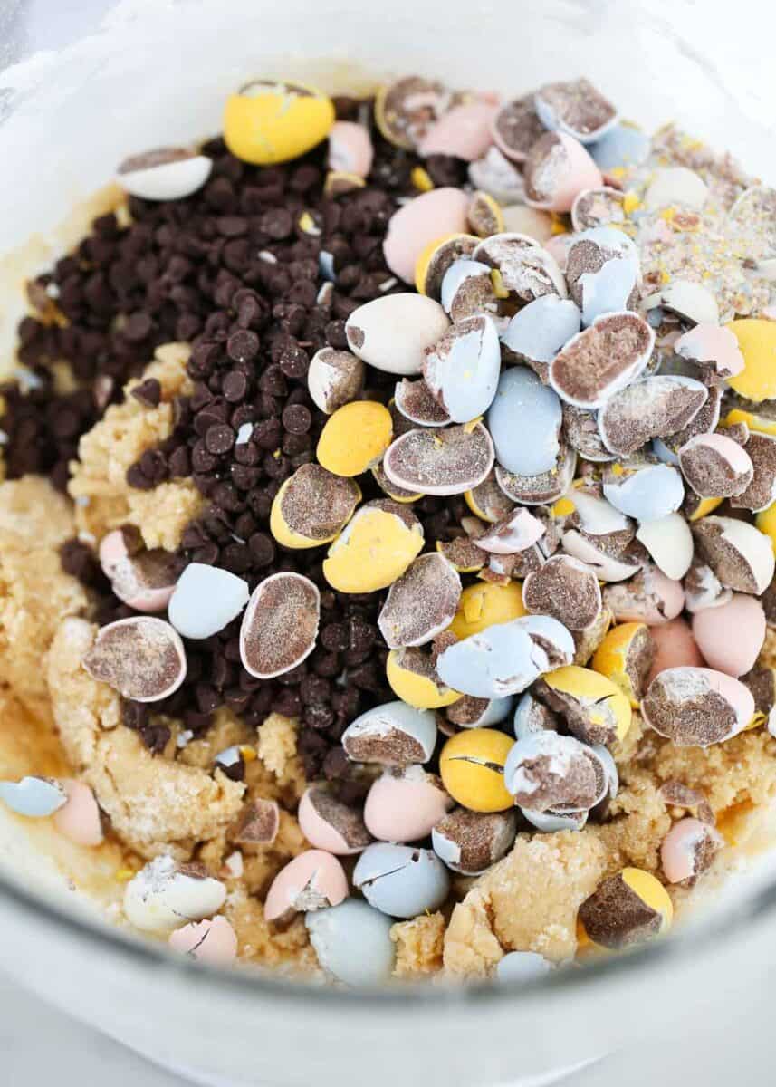 Cookie dough topped with mini chocolate chips and crushed Cadbury Mini Eggs before mixing for Cadbury egg cookies.