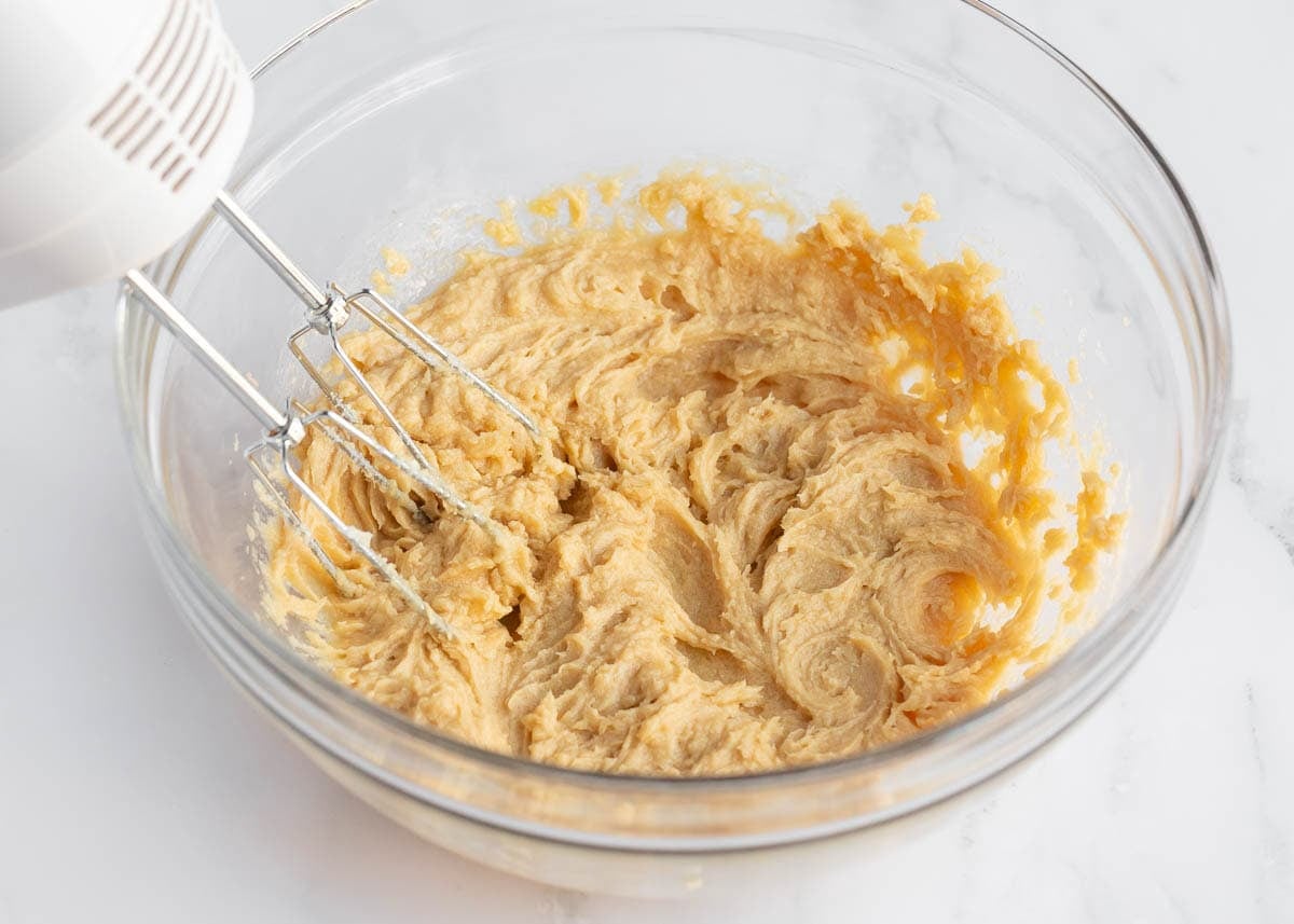 Creamed butter and sugars mixed in a glass bowl with a hand mixer for mini Cadbury egg cookies.