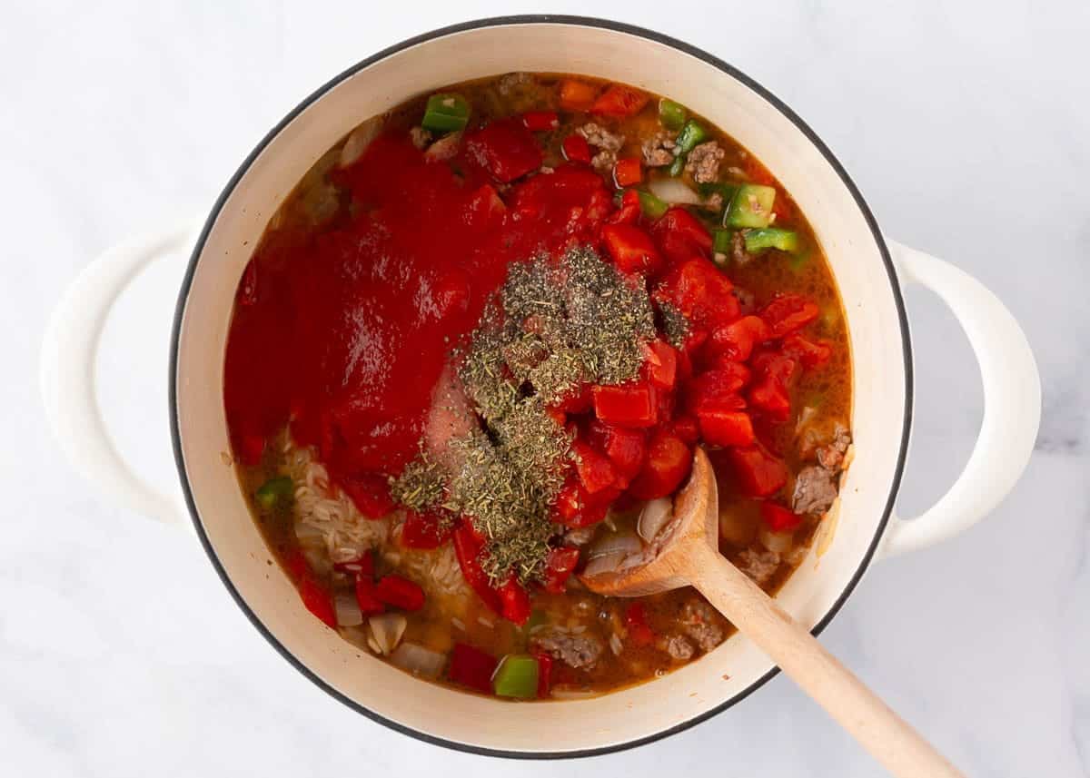 Diced tomatoes, tomato sauce, jasmine rice, broth and Italian seasoning added to the beef and peppers in a white pot, before stirring together.