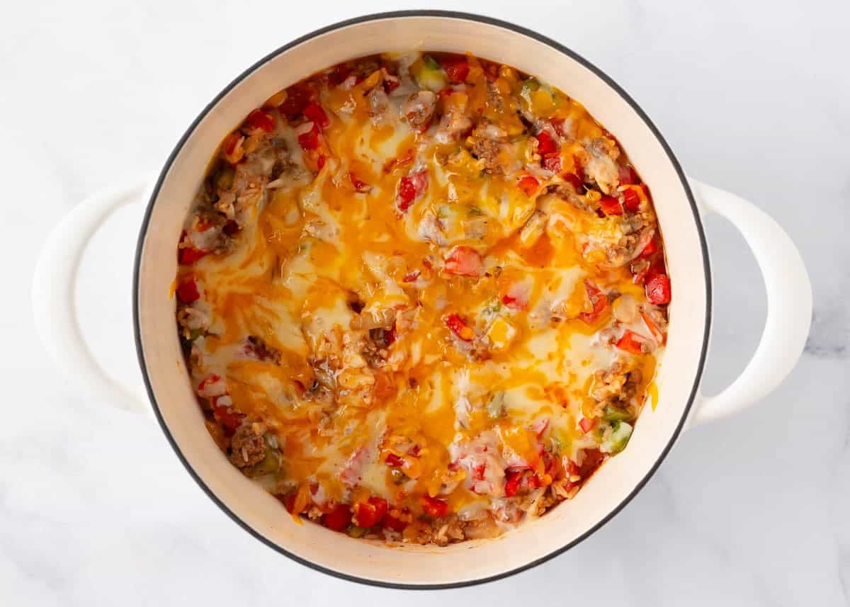 Melted cheddar and mozzarella cheese over the top of stuffed pepper casserole in a white pot, golden and bubbly.