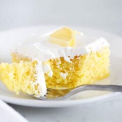 Lemon jello poke cake on a plate with a fork taking a bite showing bright lemon and moist texture.