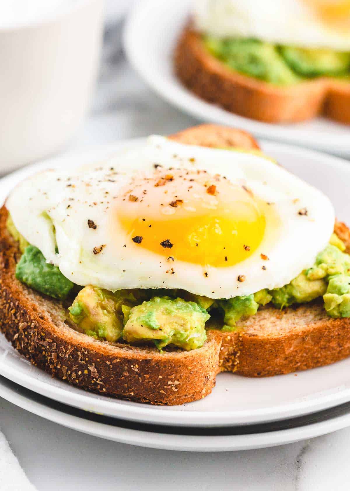 How to make sunny side up eggs perfectly every time with creamy, runny yolk and lightly cooked, pan-fried egg white. Enjoy for a protein filled breakfast or top avocado toast and bowls! Sunny side up eggs on avocado toast.