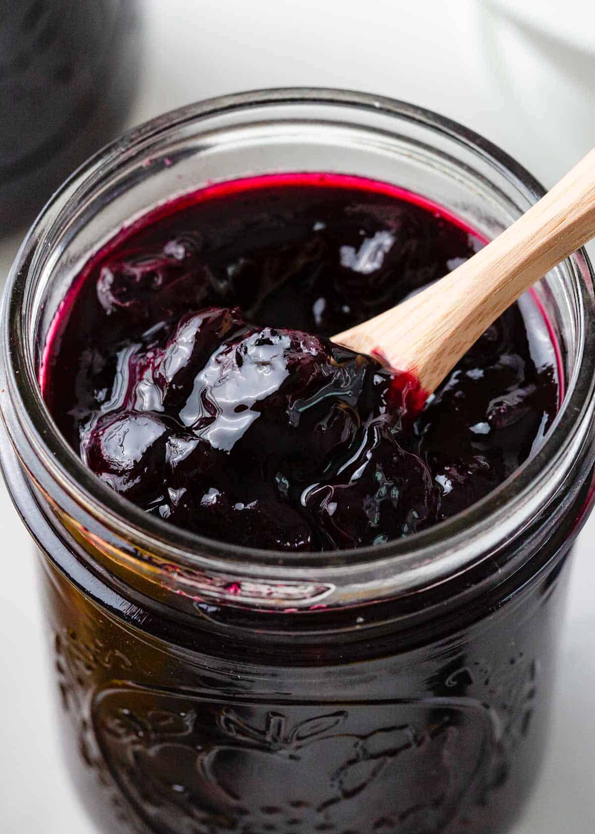 A closeup photo of blueberry jam in a glass jar.