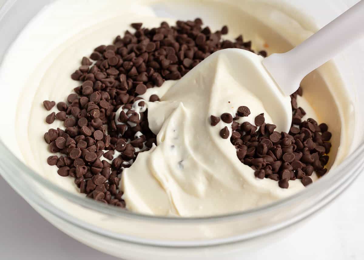 Chocolate chips being folded into cannoli dip with a spatula.