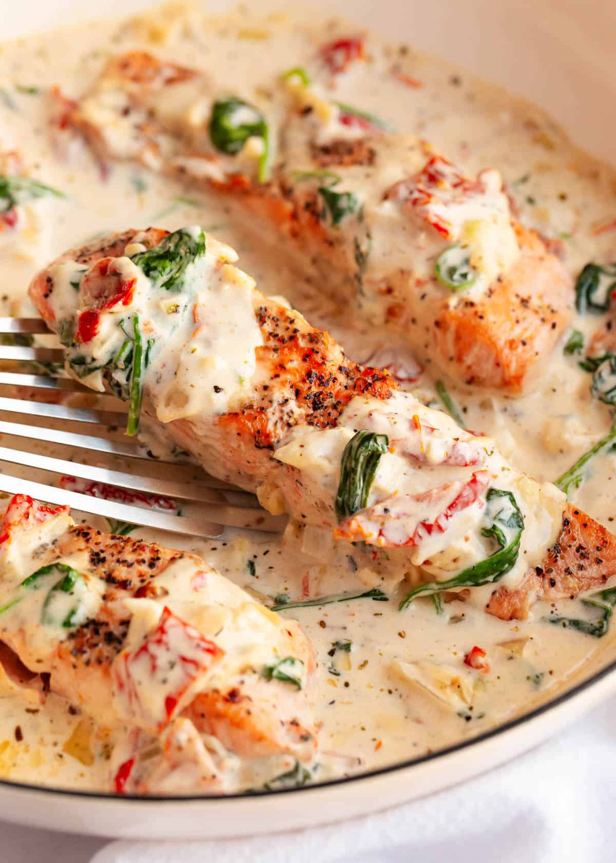 This creamy Tuscan salmon is made with pan-seared salmon fillets smothered in a creamy sundried tomato and spinach sauce. Perfect for special occasions or weeknights! Tuscan salmon in a skillet.