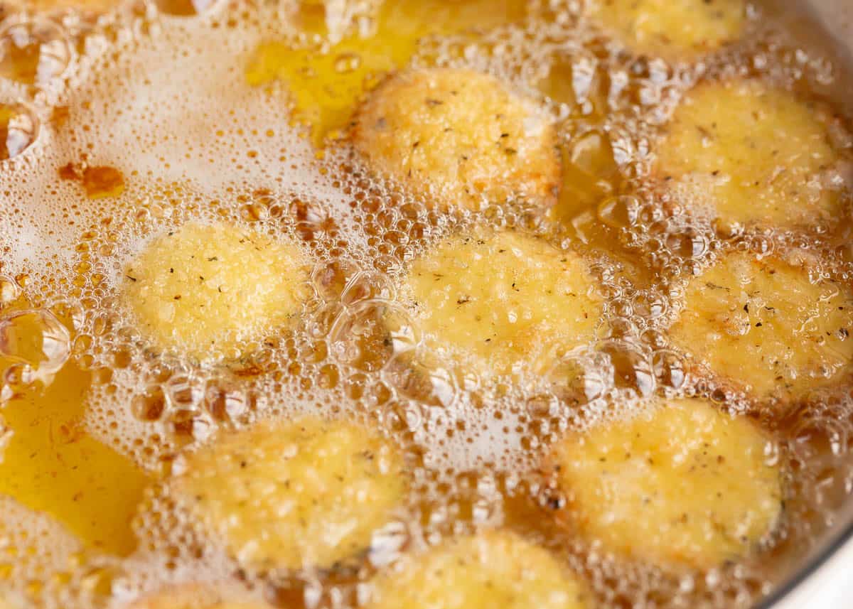 Breaded zucchini rounds frying in hot oil with golden edges and bubbles around them.