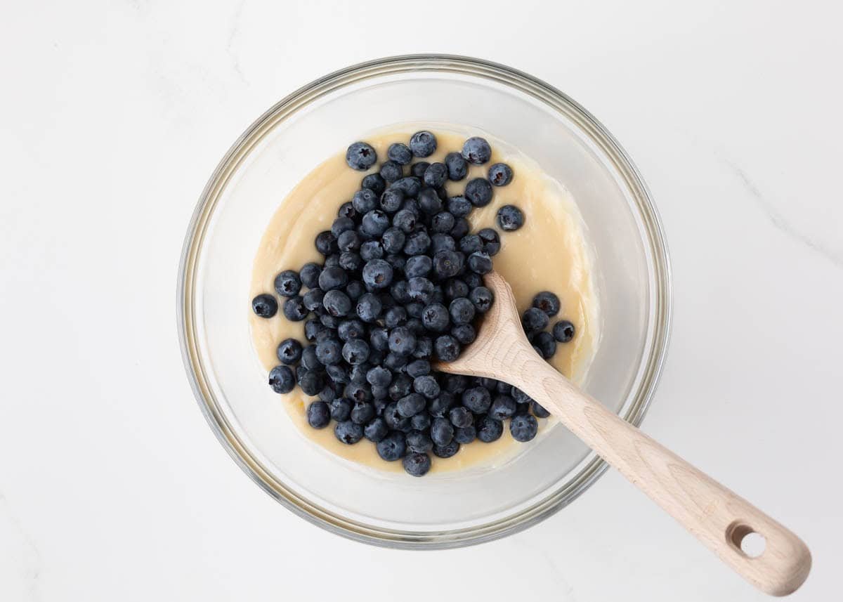 Adding blueberries to coffee cake batter in a bowl.