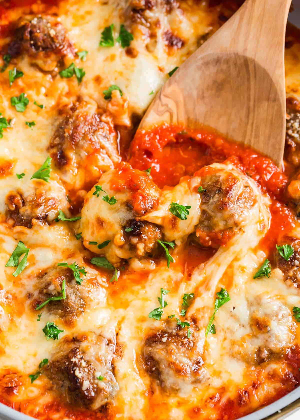 Seared until brown then smothered with marinara sauce and mozzarella cheese, these chicken parmesan meatballs will have everyone dancing to the dinner table! Chicken parmesan meatballs in skillet with serving spoon.