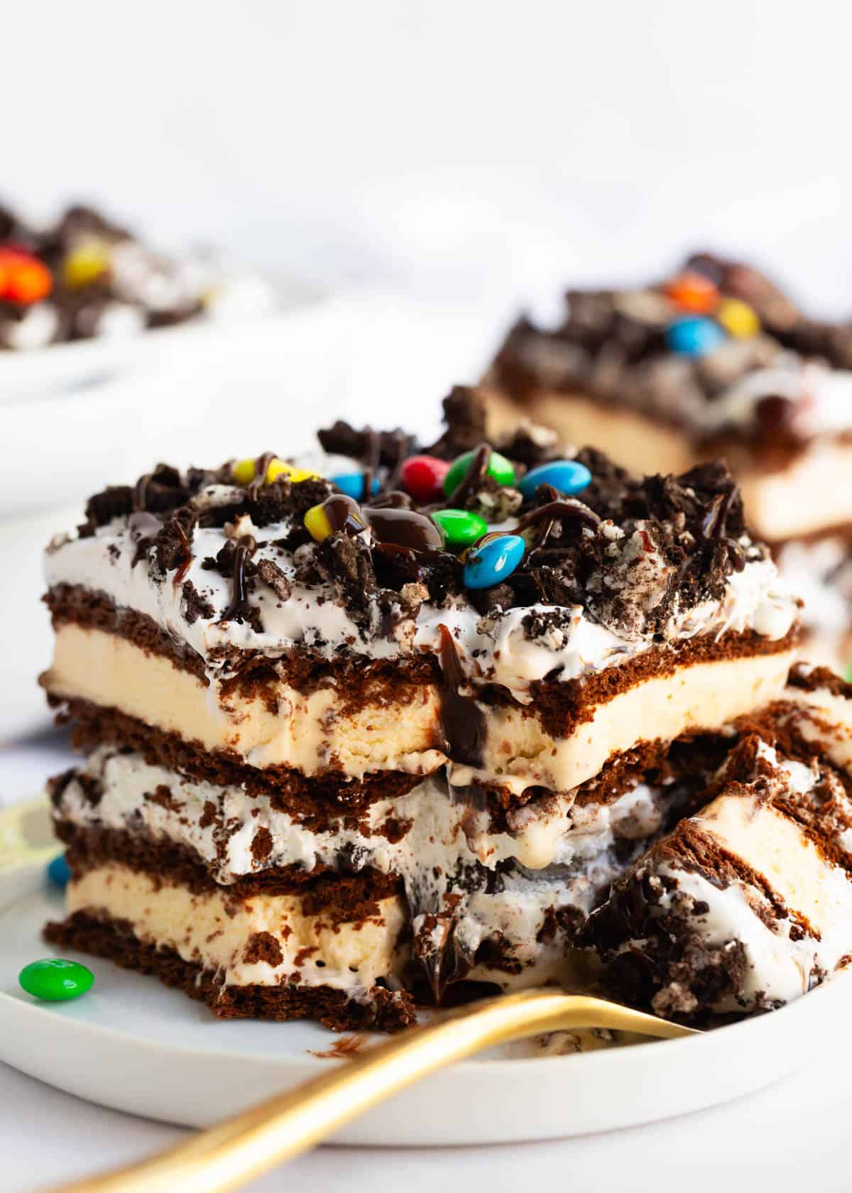 This ice cream sandwich cake is the best summer dessert! It's easy to make this no-bake treat with ice cream sandwiches, hot fudge sauce, Oreo's and Cool Whip. A slice of ice cream sandwich cake on a plate.