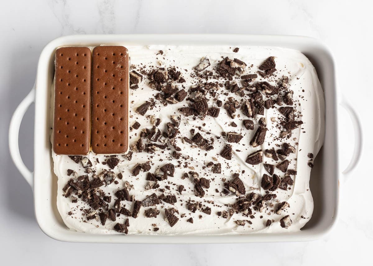 This ice cream sandwich cake is the best summer dessert! It's easy to make this no-bake treat with ice cream sandwiches, hot fudge sauce, Oreo's and Cool Whip. Showing how to make ice cream sandwich cake.