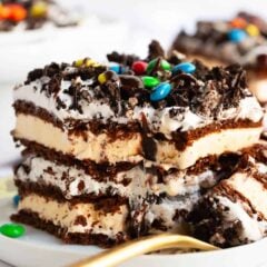 Slice of ice cream sandwich cake on a white plate with M&Ms, Oreo crumbles and hot fudge.