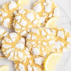 Lemon crinkle cookies on parchment covered cooling rack with fresh lemon slices.