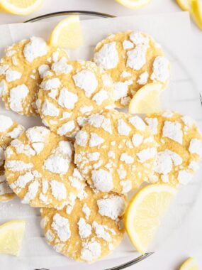 Lemon crinkle cookies on parchment covered cooling rack with fresh lemon slices.