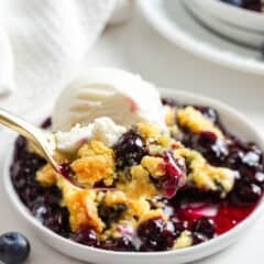 Spoonful of blueberry dump cake with blueberry pie filling and vanilla ice cream in a white bowl.