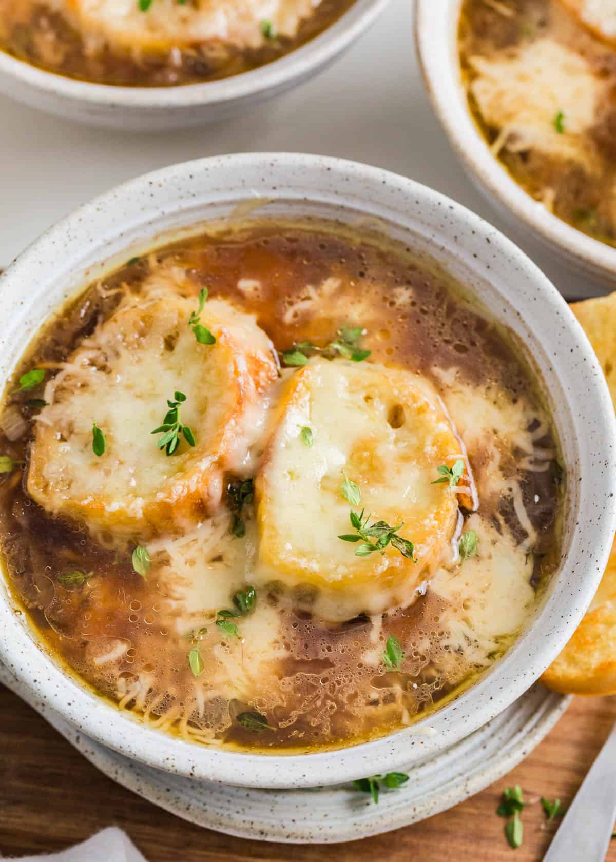 This French onion soup is easy to make with soft, sweet caramelized onions simmered in a flavorful beef broth topped with slices of crispy baguette and plenty of melted Gruyere. French onion soup in a white bowl.
